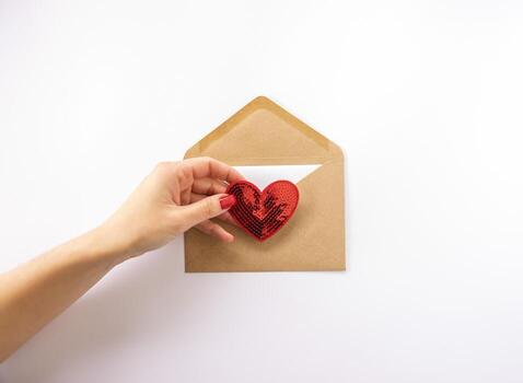 A woman holding a red heart in her hand and sending in in an envelope for Valentines Day photo