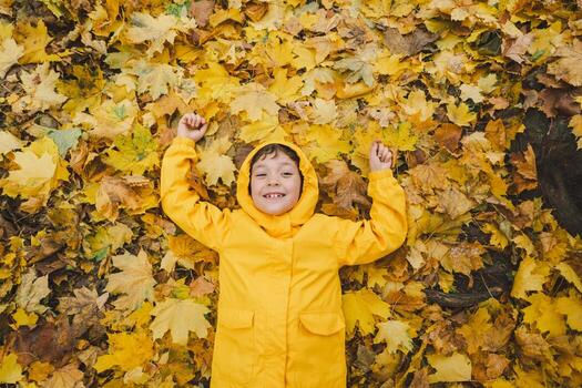 Joyful Child in Yellow Raincoat Laying in Autumn Leaves at a Park photo