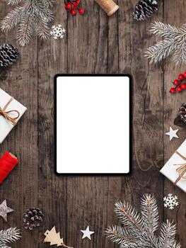 Vertical flat lay with tablet and blank screen on rustic wooden background decorated with pine cones, branches, stars, and Christmas gifts photo